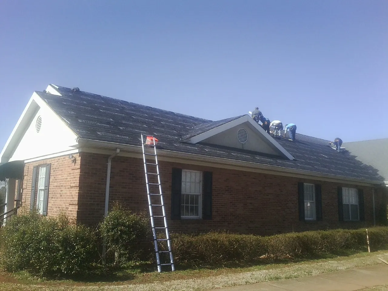 Crew tearing shingles off a brick ranch roof with a ladder set — Metal Roof Repair work by our crew in Phenix City
