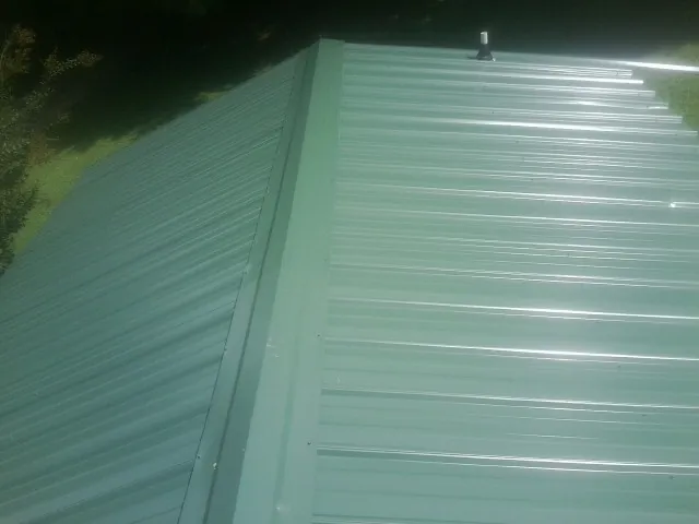 New green metal panels meeting at the ridge of a roof — Flat Roof Repair work by our crew in Phenix City