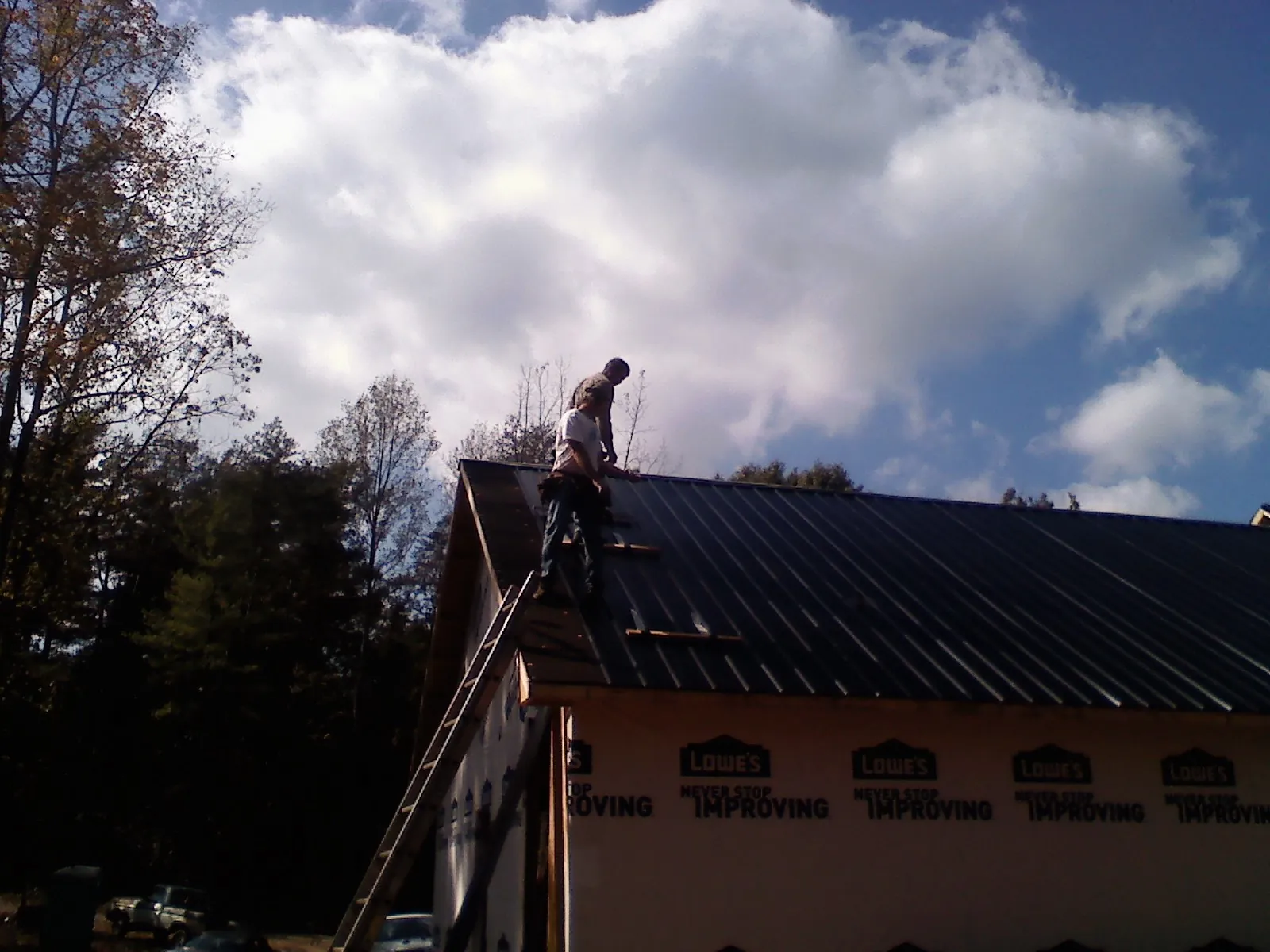 Roofer fastening dark metal panels high against a cloudy sky, from a Roof Inspection job in Phenix City