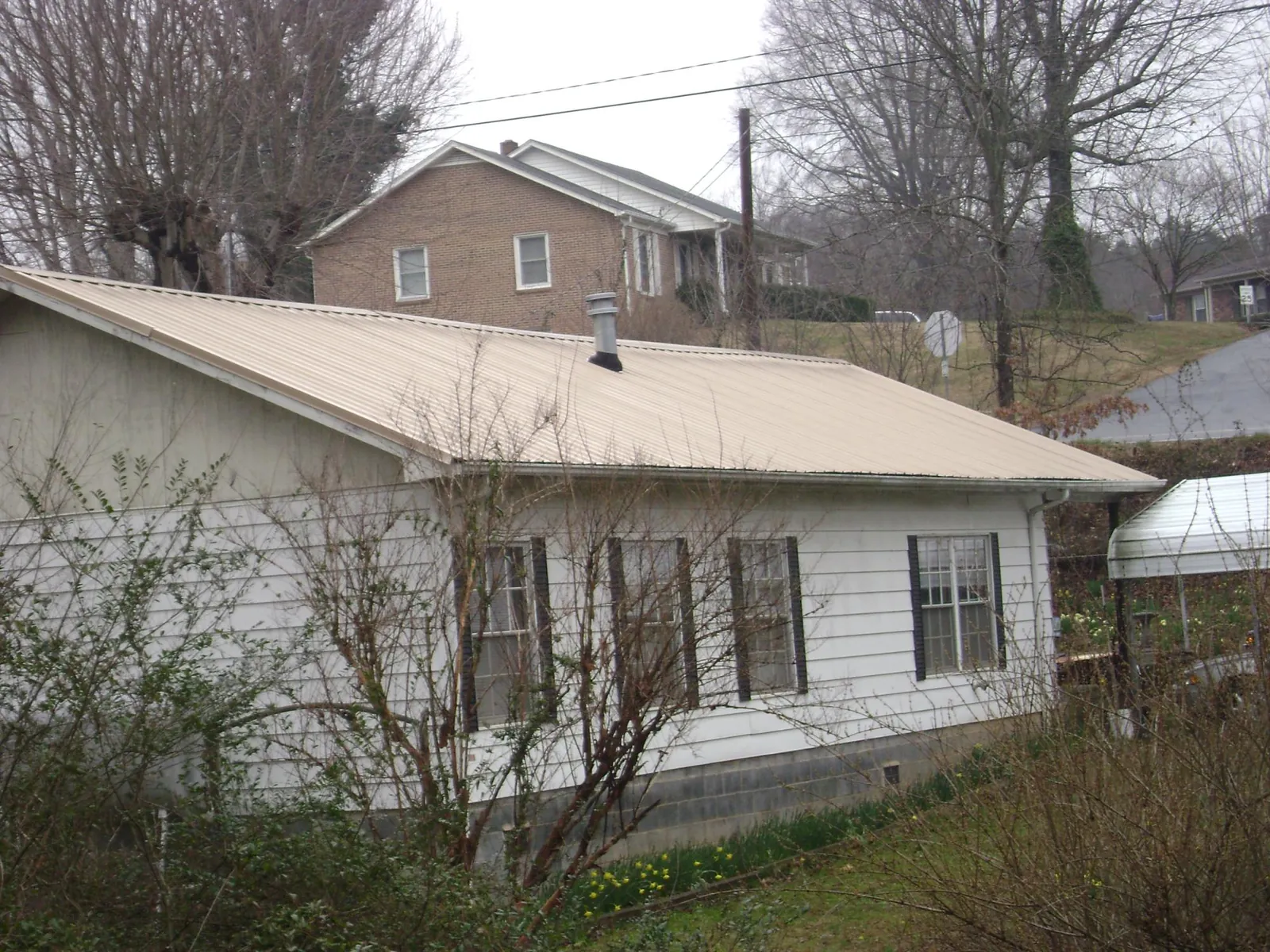 Tan metal roof on a white sided house set into a hillside — Commercial Roofing by Roofing Brothers in Phenix City